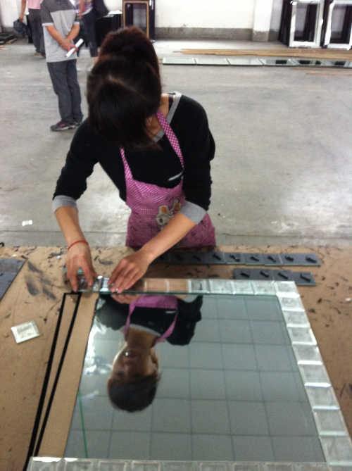 Woman at a factory assembling the outer part of a mirror