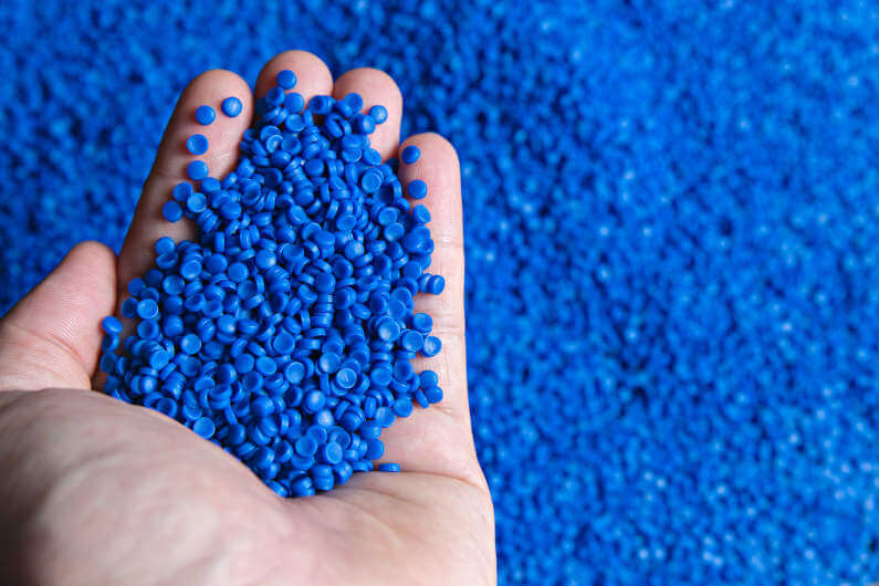 Hand holding blue plastic polymer granules