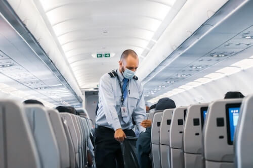 Male flight attendant wearing surgical mask and collecting trash from passengers