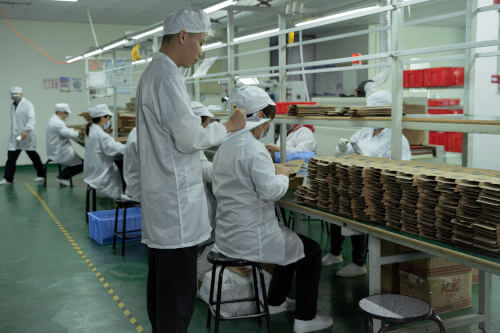 Auditor with clipboard in factory observing workers